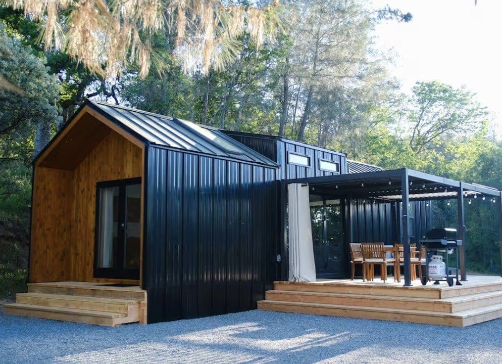 Black-and-cedar ADU with a wide deck and a covered pergola, set among trees