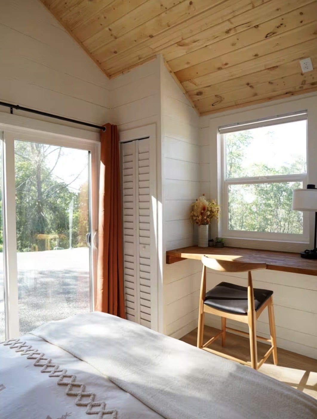 Bedroom in a finished build with a pine ceiling, a built-in desk under the window and a sliding glass door