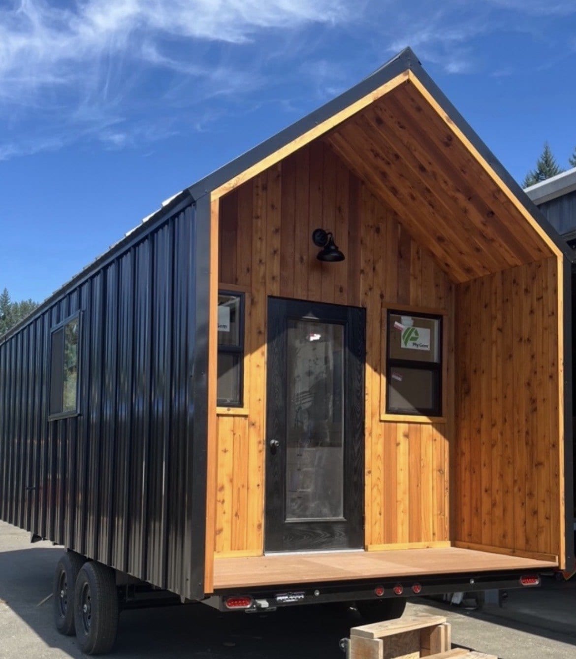 Tiny home in black metal siding with a cedar-lined gable porch and a glass front door