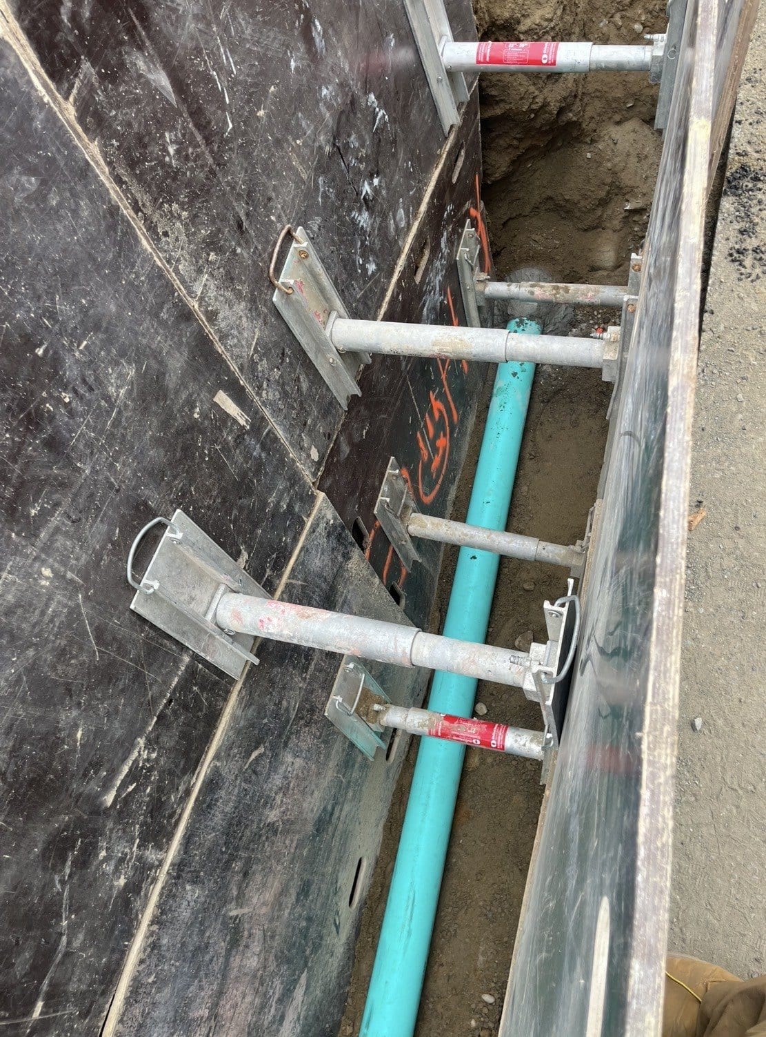Open utility trench along a foundation wall, with new utility lines run up through the footing